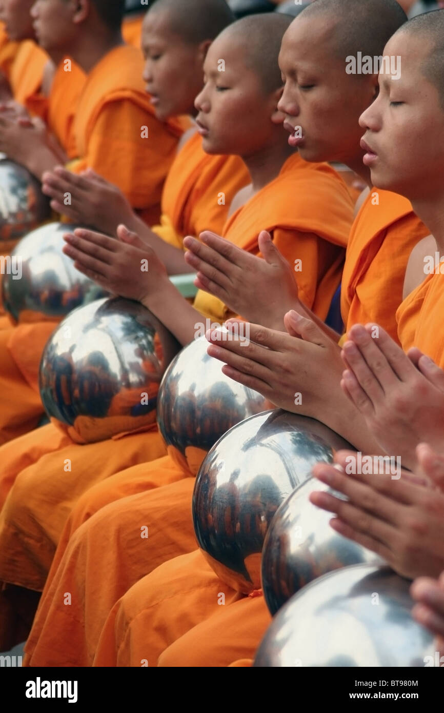 Buddhist monks wearing orange robes are praying with their alms bowls near Tha Pae Gate in
