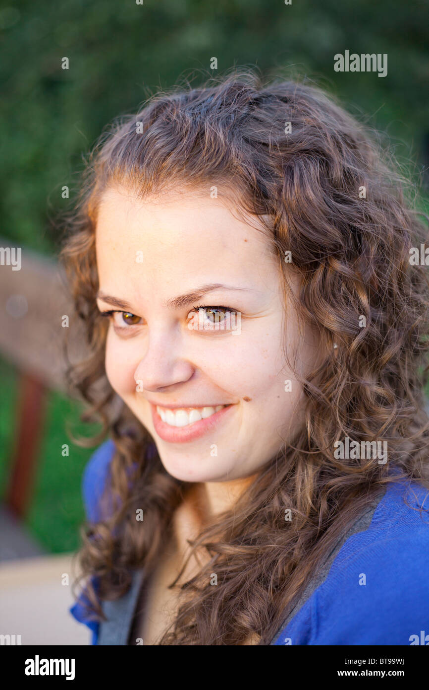 Young woman with curly hair smiling warmly at the camera in an outdoor ...