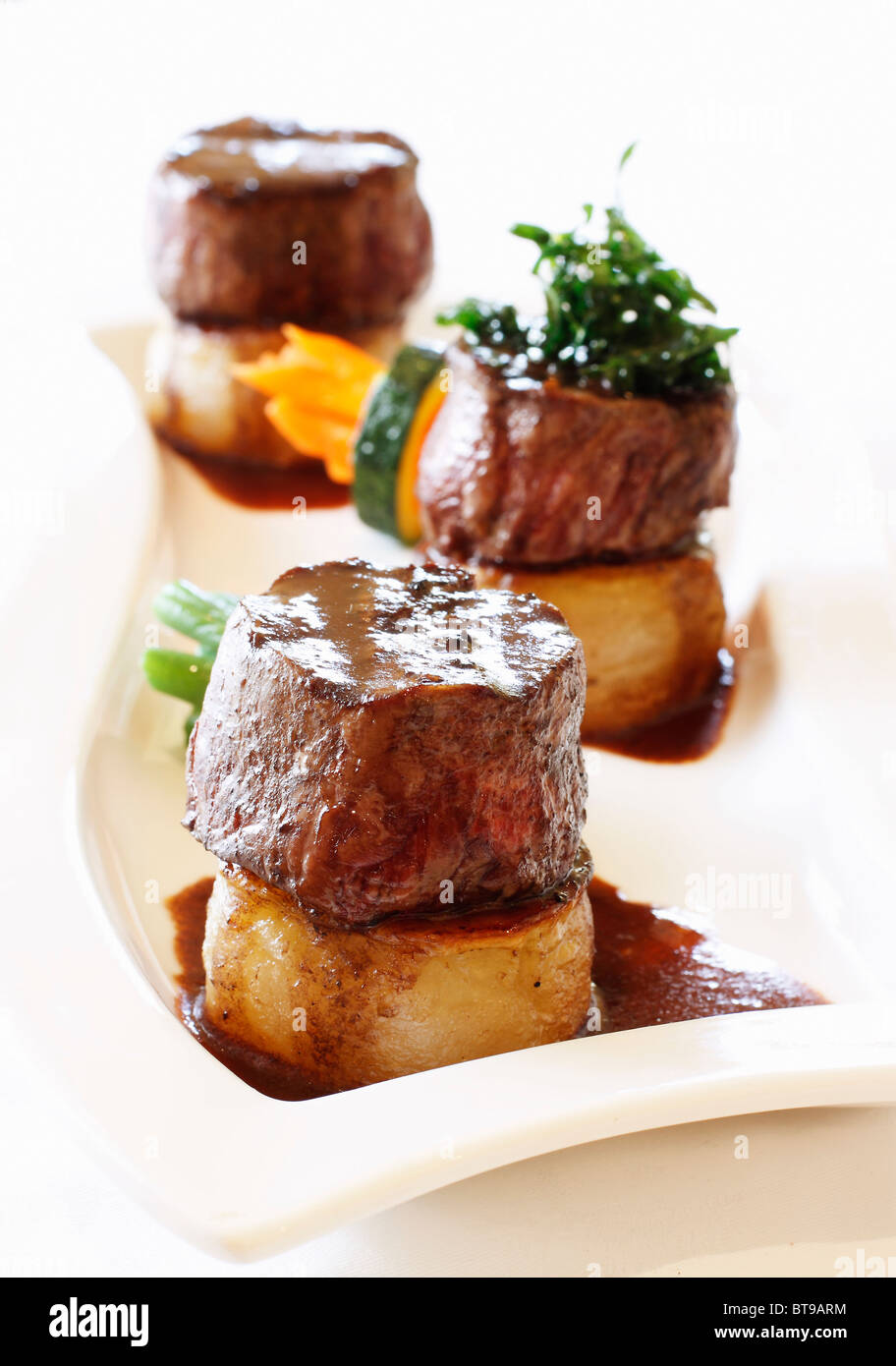 Beef Medallions on Potatoes with Gravy and Vegetables on a While Plate.  Full color, vertical orientation, clean, simple. Stock Photo