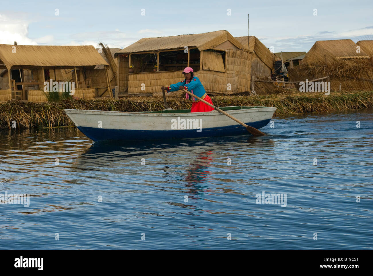 Peru, Puno, Lake Titicaca, Uros Islands, Islas Flotantes, woman rows row boat past small island Stock Photo