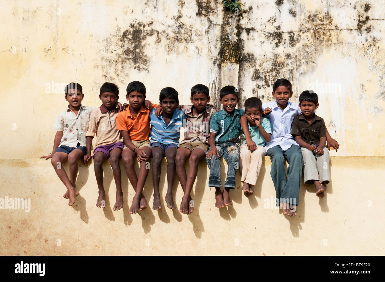 Rural South Indian village boys sitting on school wall in bright sunlight. Andhra Pradesh, India Stock Photo