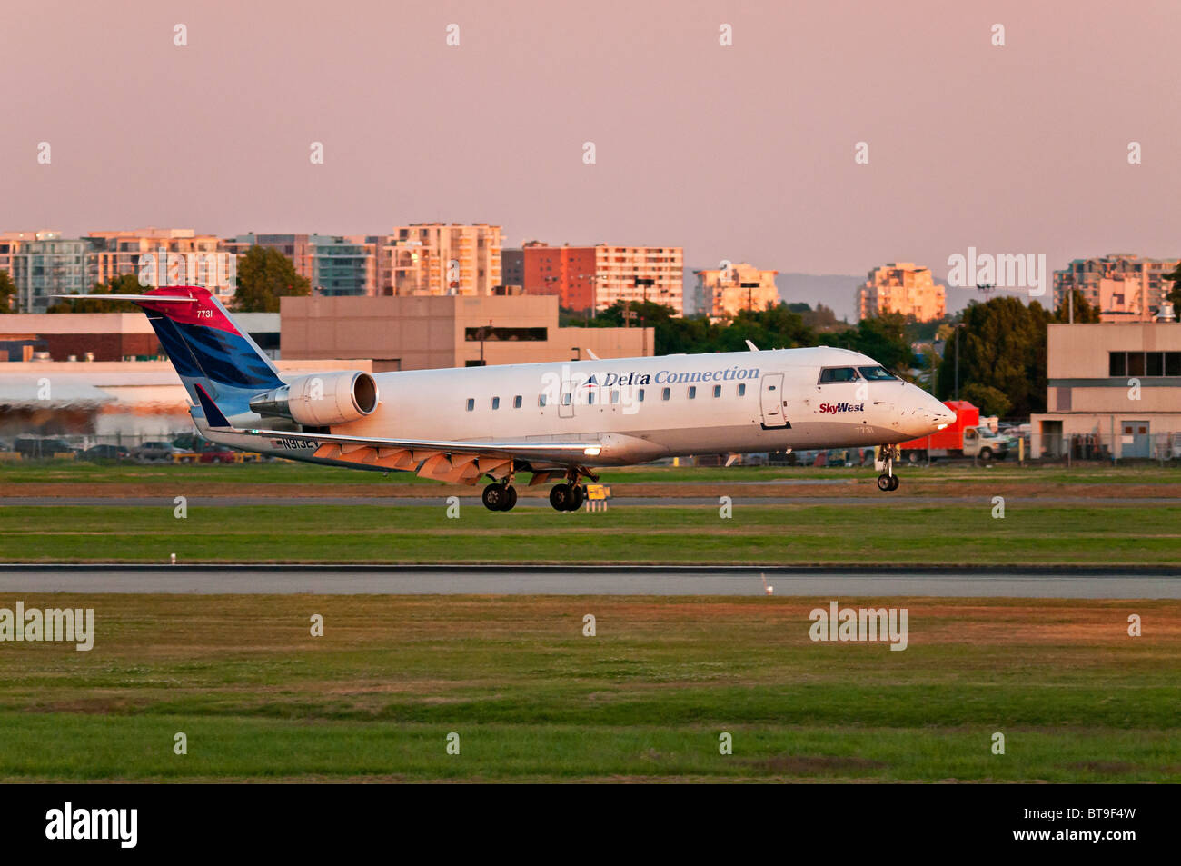 A Delta Connection (SkyWest Airlines) CRJ-200ER regional jet airliner lands at Vancouver International Airport (YVR) at sunset. Stock Photo