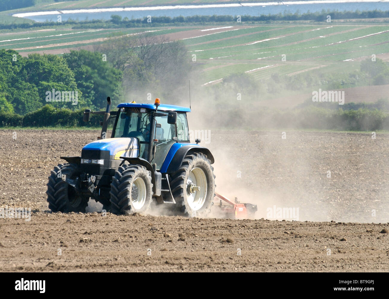 Tractor working on dry land in Sussex pulverising the soil and creating clouds of dust which is blown in the wind. Stock Photo