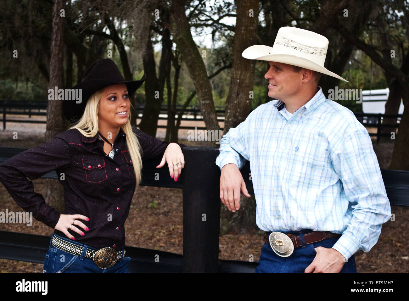Young and attractive cowboy and cowgirl talking while standing in front of a horse coral on a ranch Stock Photo