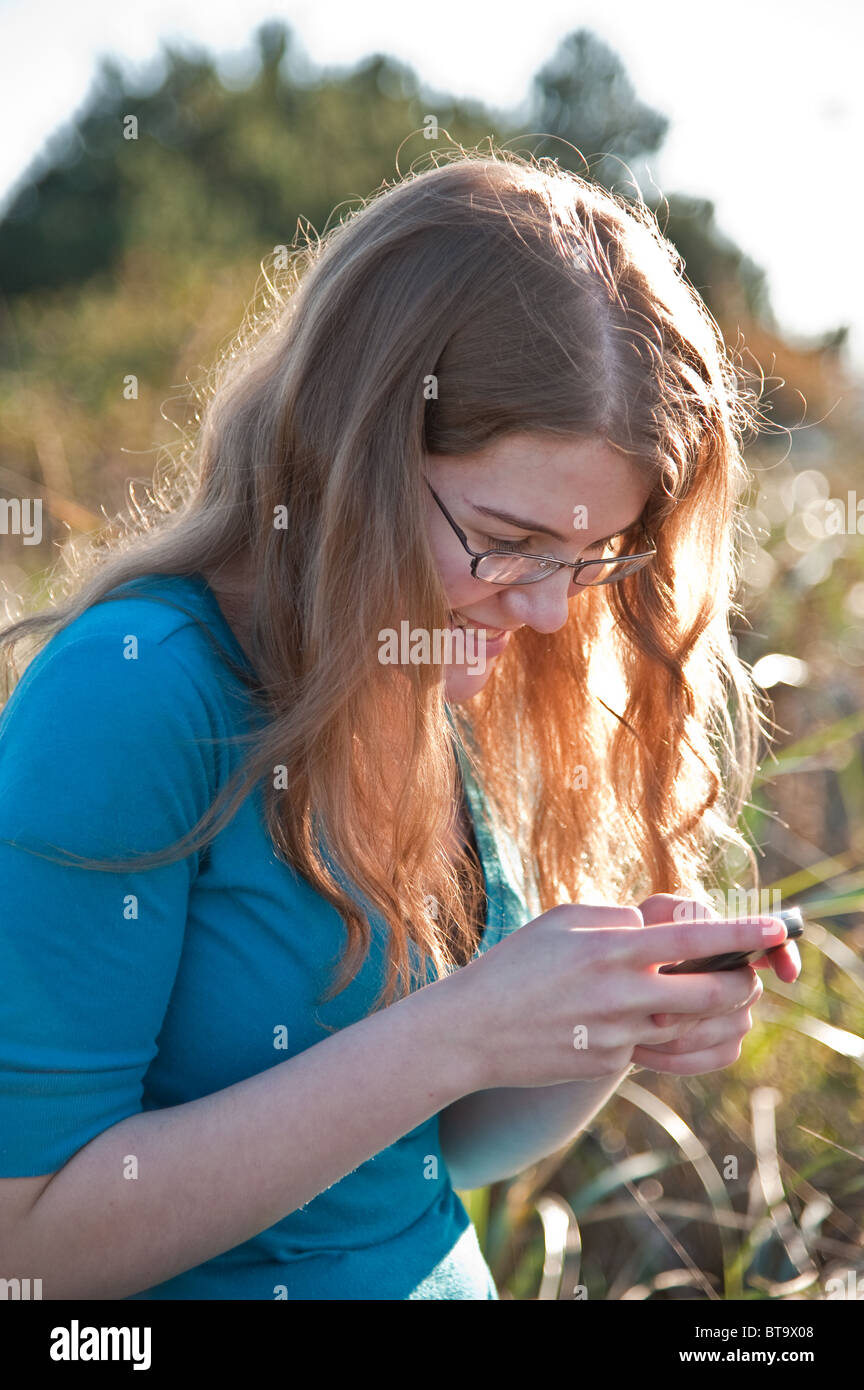 A vertical image of a young Caucasian red hair high school teenage girl checking her phone Stock Photo
