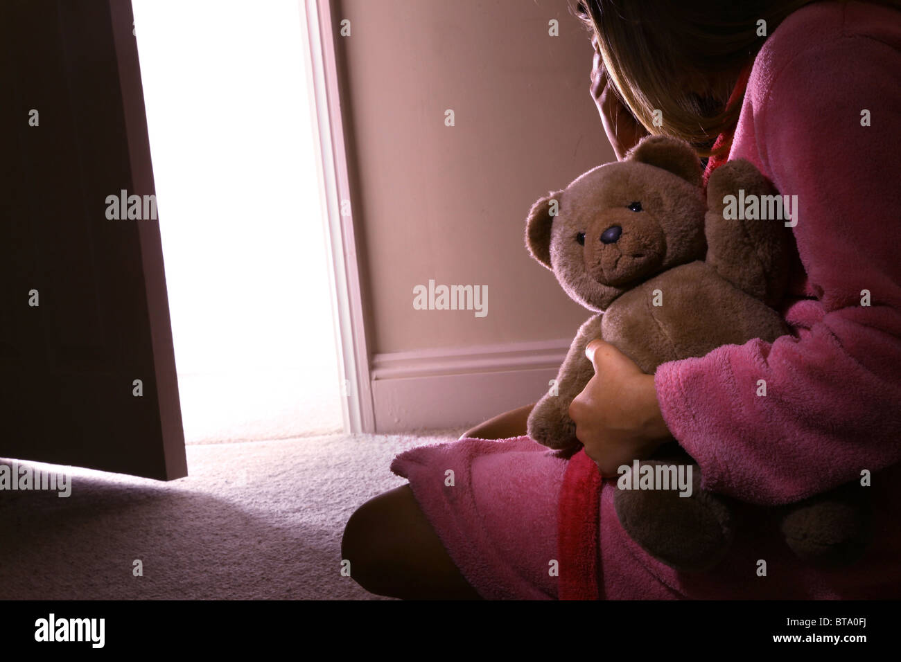Young girl sitting holding a teddy bear, back view. Stock Photo