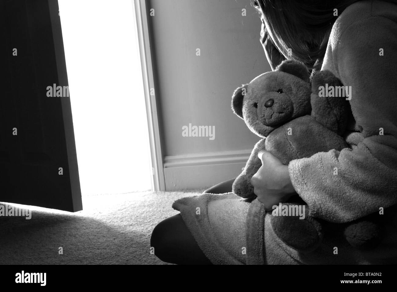 Young girl sitting holding a teddy bear, back view. Stock Photo