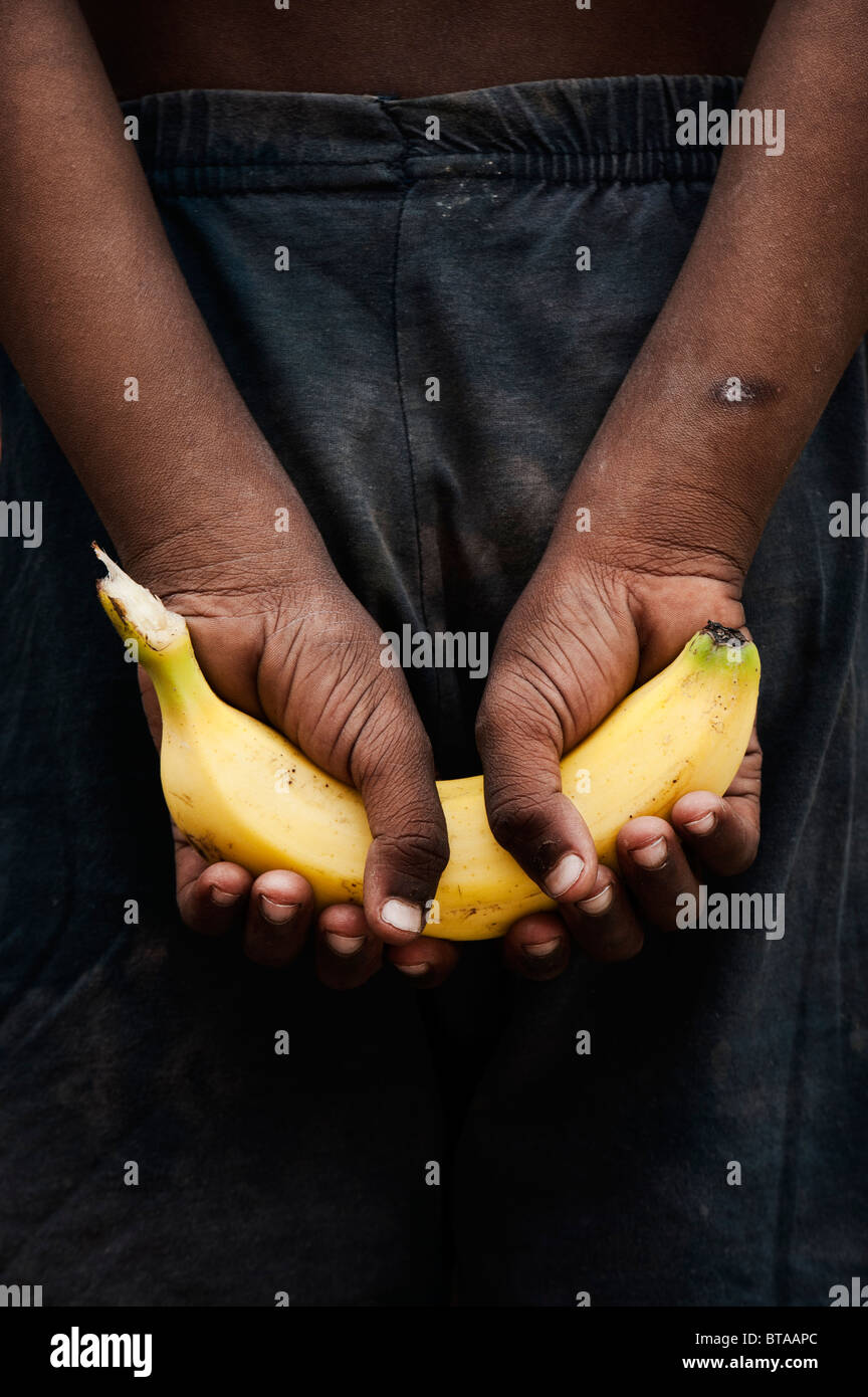 Poor Indian boy holding a banana in his hands behind his back. India Stock Photo