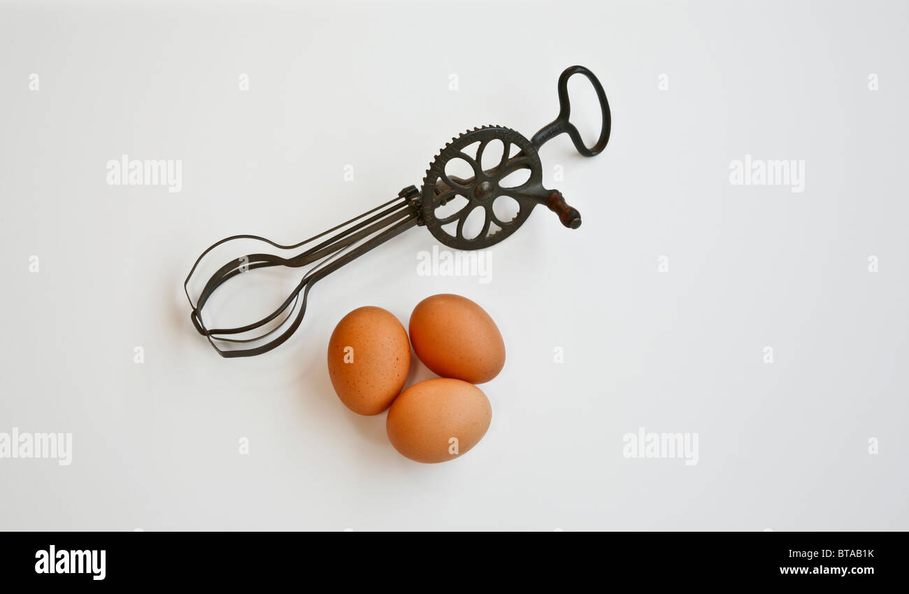 Close up of antique egg beater, vintage kitchen utensil, three brown eggs white background images, New Jersey, USA, US egg beaters, retro historical Stock Photo
