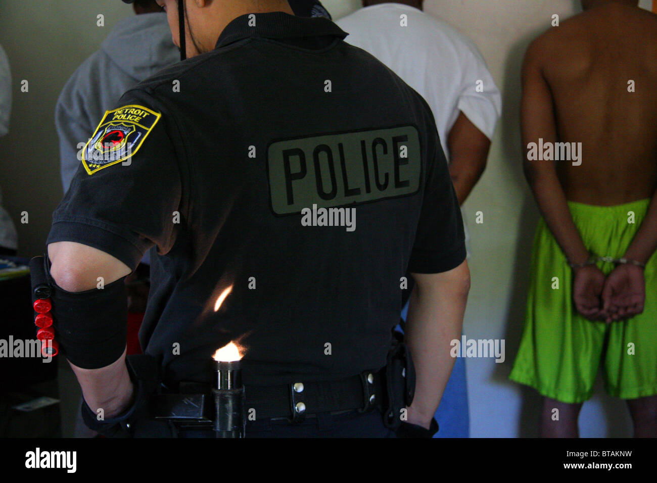 Police officer from the Detroit Police Narcotic unit with handcuffed suspects at a drug raid. Stock Photo
