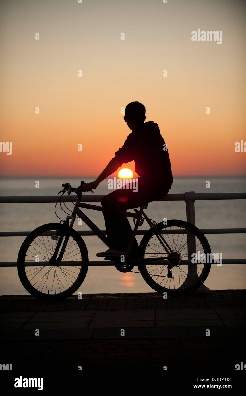 October evening - Silhouette of a boy on a bike silhouetted at Sunset over Cardigan Bay, Aberystwyth Wales UK Stock Photo