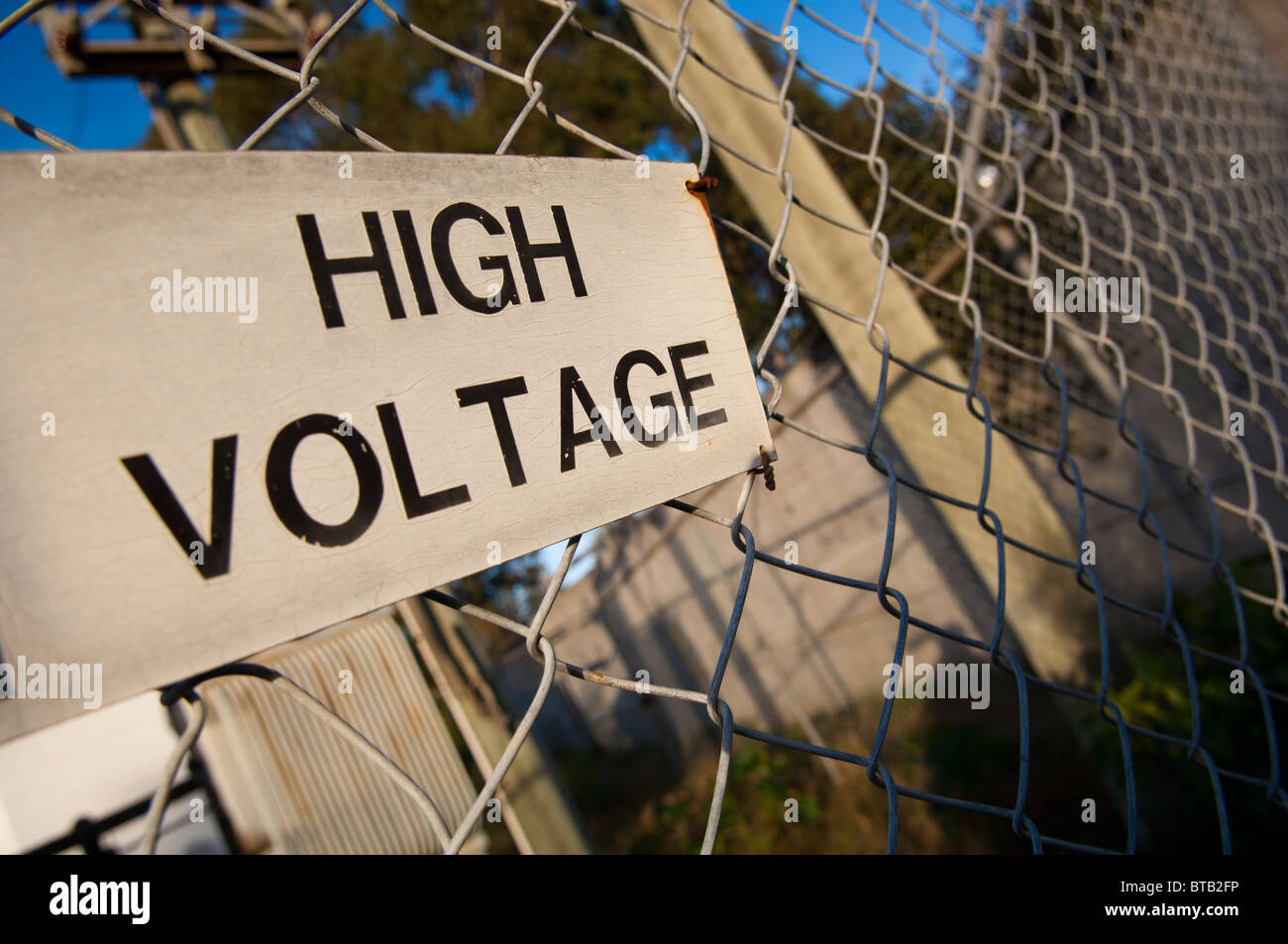 High voltage sign is aged on a wire (cyclone) fence Stock Photo