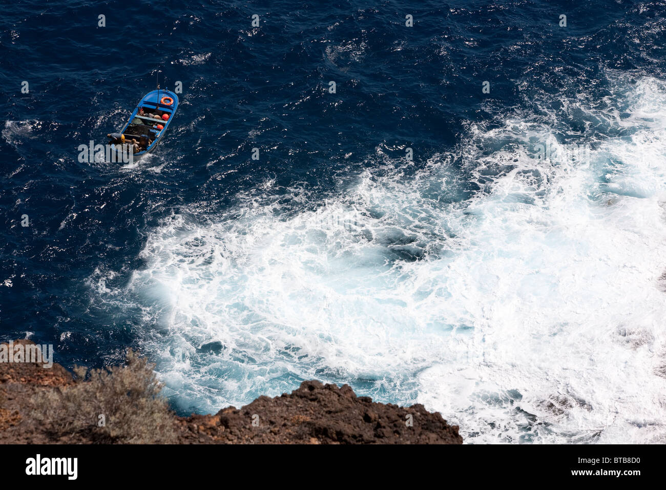 Fishing boat in ocean of rough seas and white water close to rocks. Stock Photo