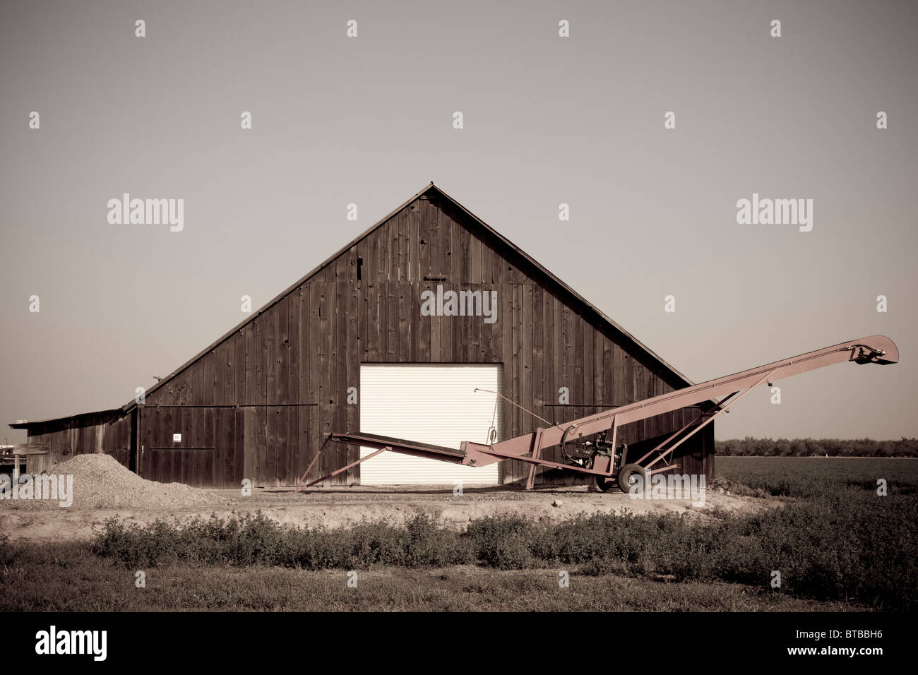 An old barn with a new door and a conveyor out front in Modesto California Stock Photo
