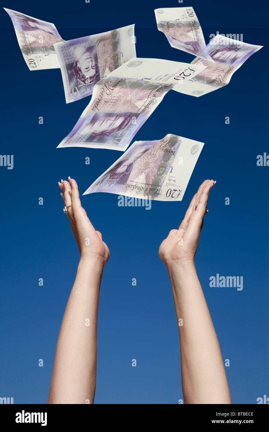 Womans hands stretching up to catch £20 notes falling from a blue sky Stock Photo