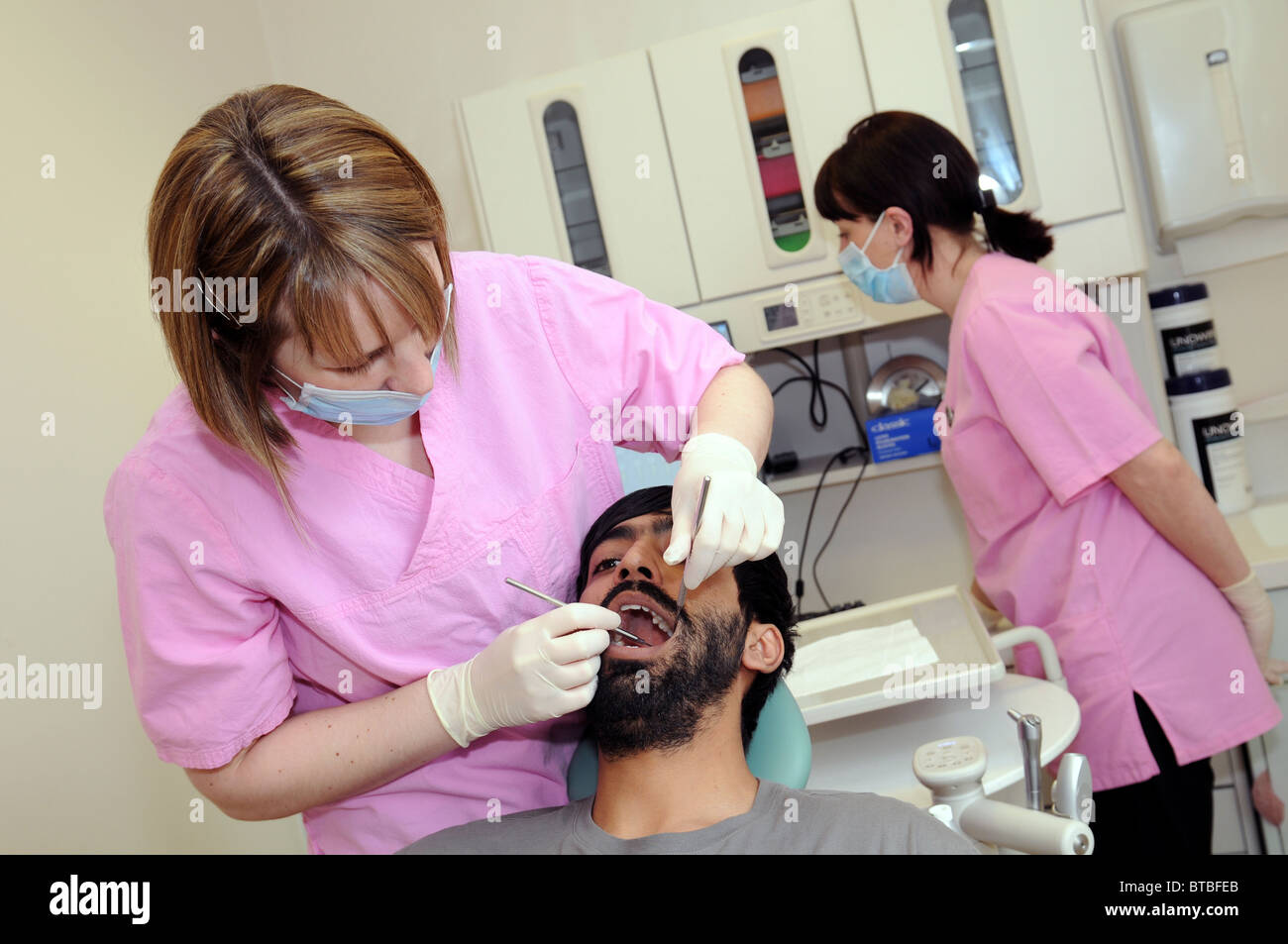 A female dentist examining a male patient's teeth in a dental surgery Stock Photo