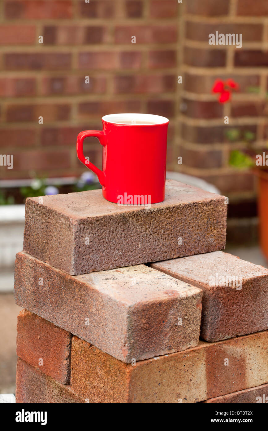 A builders cup or mug of hot tea on top of a pile of bricks Stock Photo