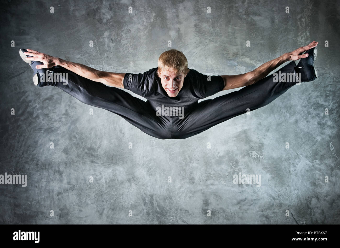 Young man dancer jumping up high. On wall background. Stock Photo