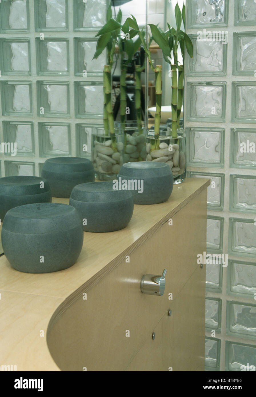 Gray lidded pots beside glass vase with foliage on pale wood shelf ...