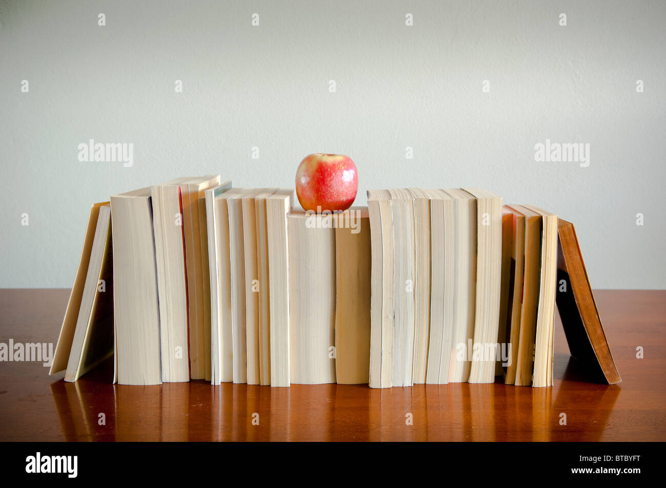 A row of books with an apple on top sits on a timber table with blank space behind Stock Photo