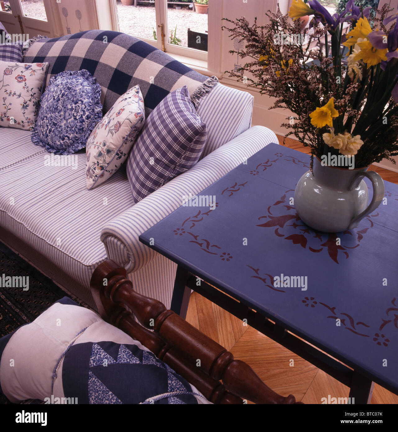 Vase of flowers on bright blue table with stenciled decoration beside ...