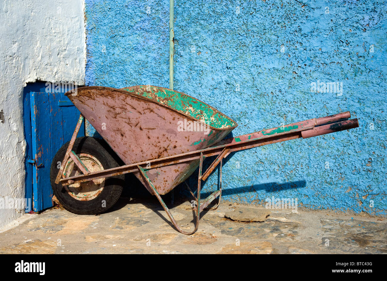 Still life of an old wheelbarrow against a light blue adobe wall. Taken on the Greek island of Amorgos. Stock Photo