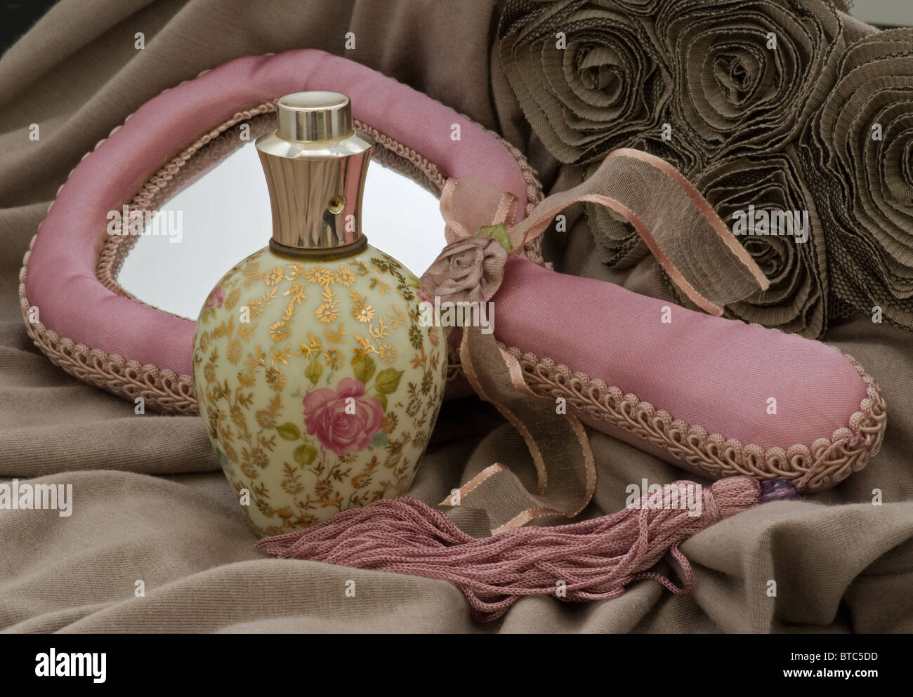 Perfume bottle atomizer with hand mirror in pink on sculpted fabric background. Stock Photo