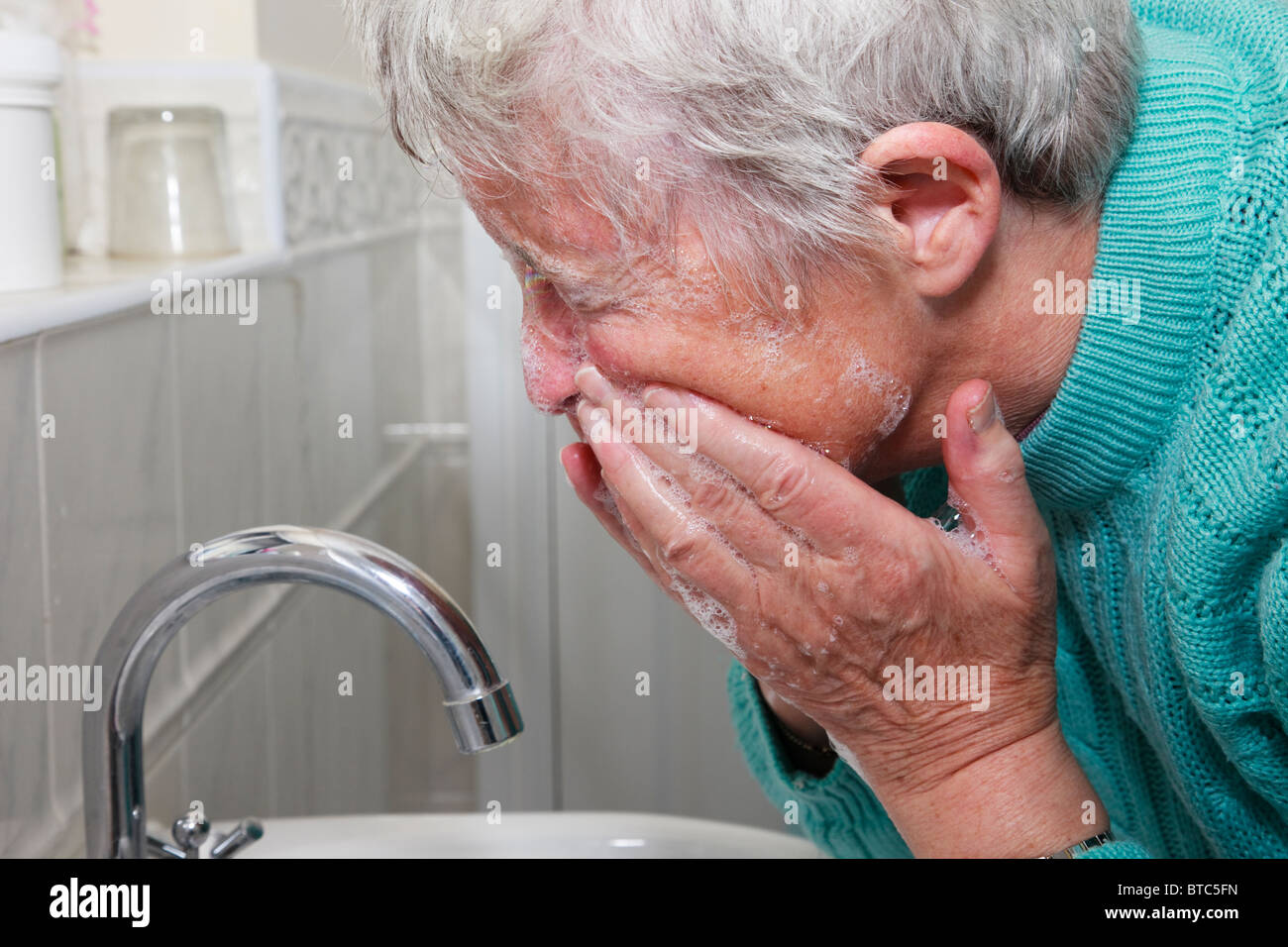 Senior woman washing face with soap and water in a bathroom. England UK