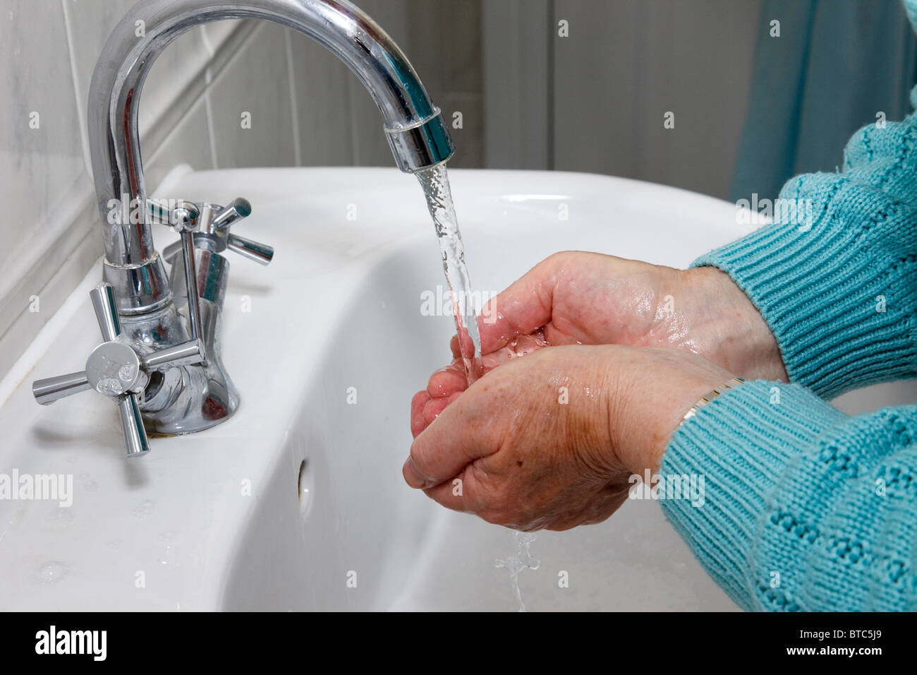 A senior elderly woman cleans by washing hands thoroughly under running tap water in a handbasin to protect against disease. England UK Britain Stock Photo