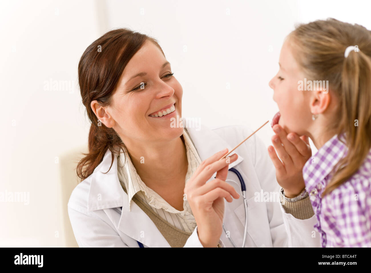 Female doctor examining child with tongue depressor at surgery Stock