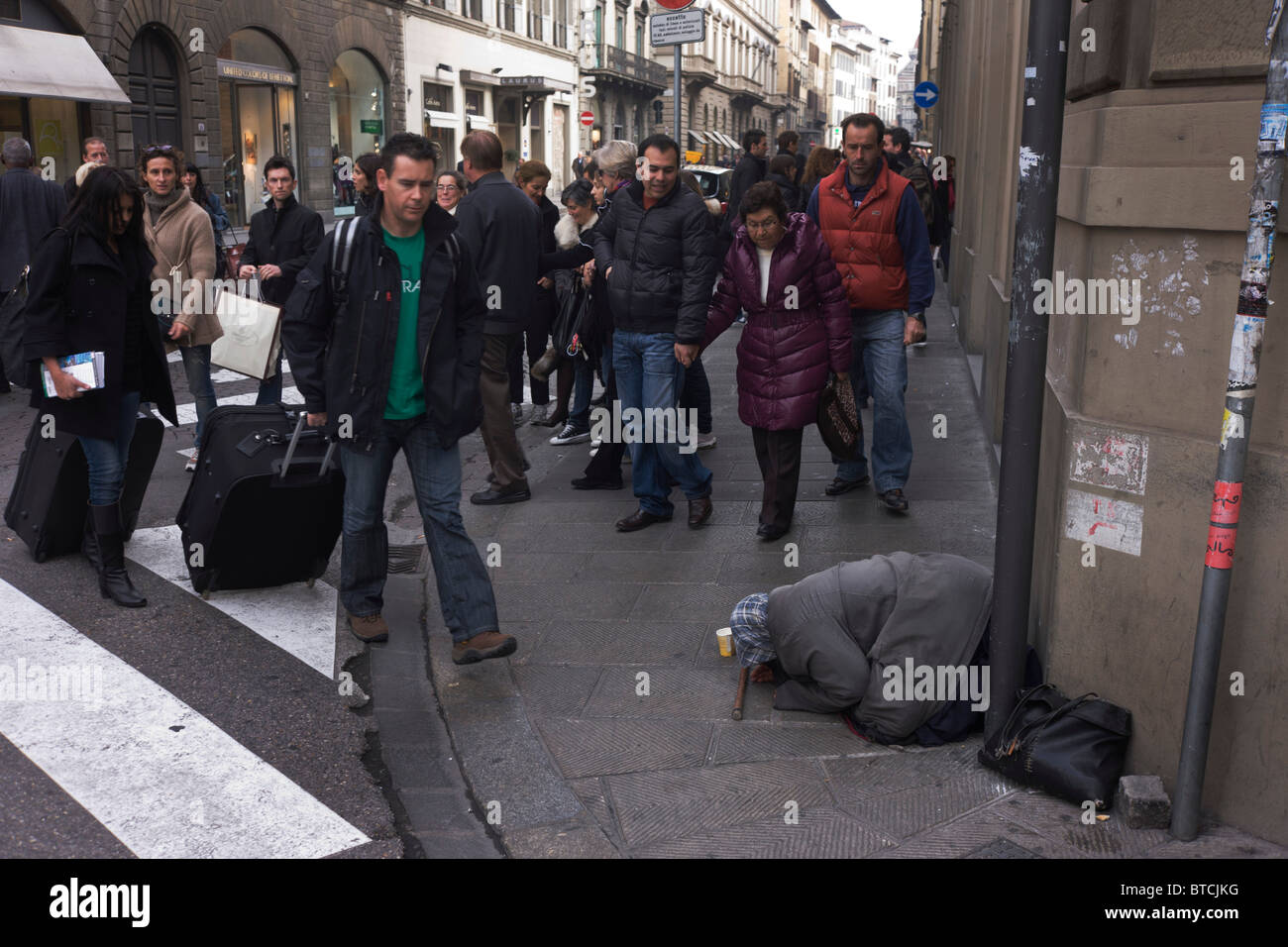Street beggar ignored by Italian shoppers and pedestrians on Florence pavement. Stock Photo
