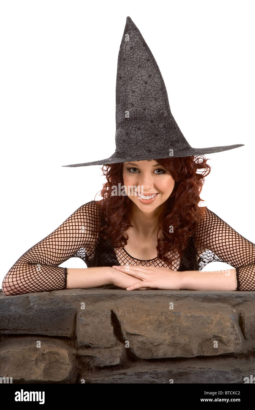 Portrait of Hispanic teenager girl in black Halloween hat and fishnet dress by stone fence Stock Photo