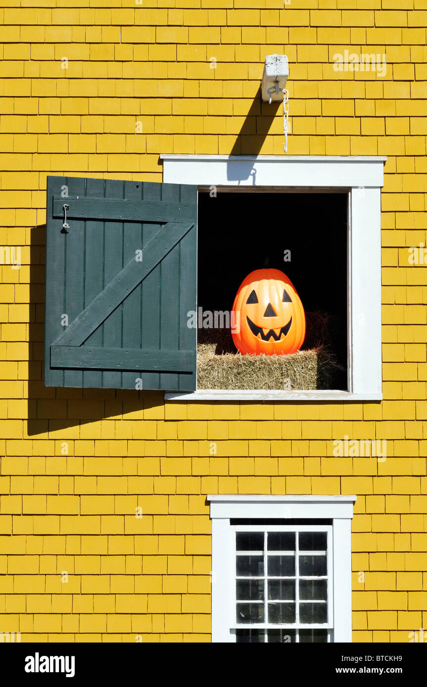 Orange smiling Jack O'Lantern on a bale of hay  inside a barn with door open on a sunny day. Stock Photo