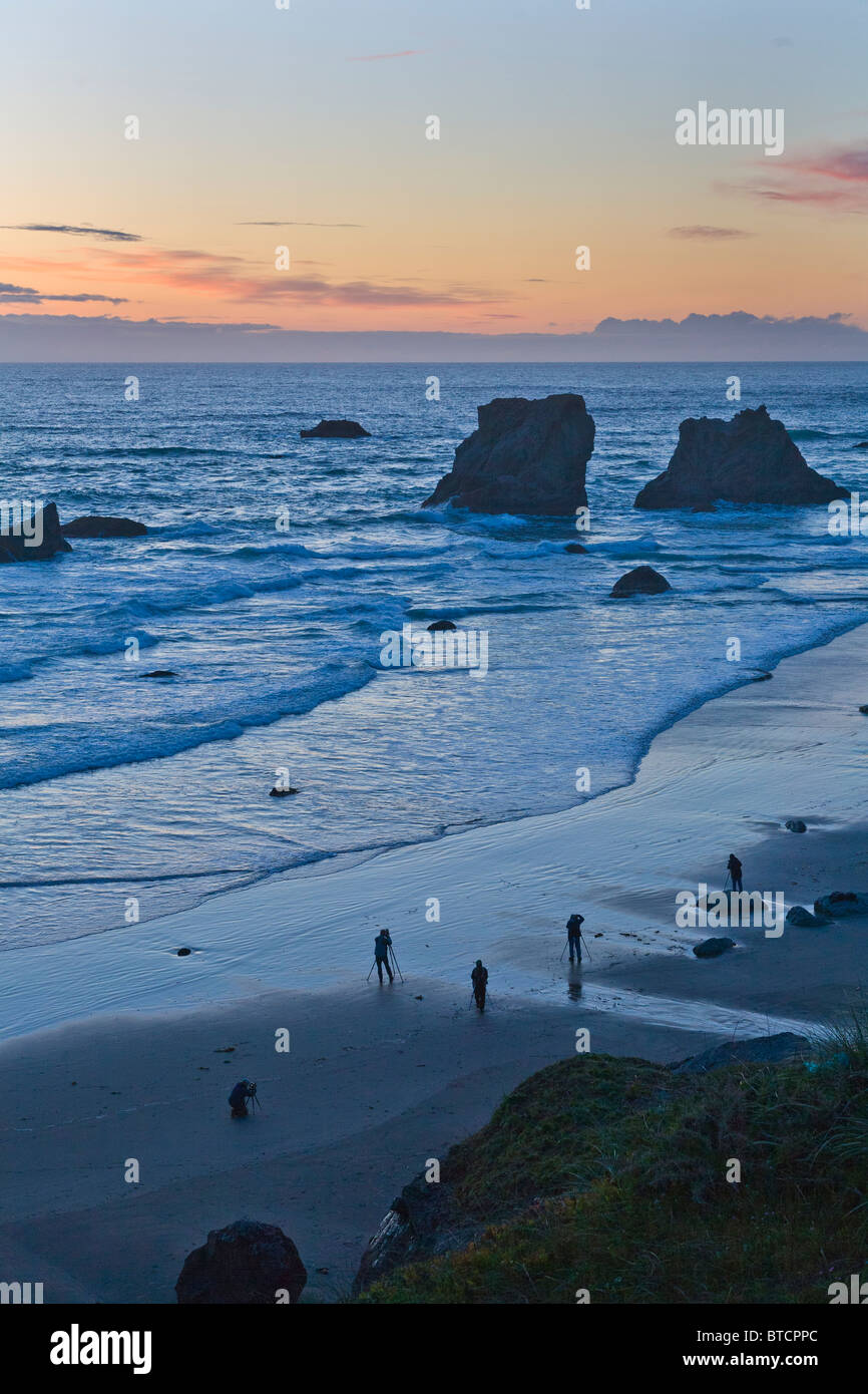 Photographers silhouetted on Bandon Beach at sunset with seastacks on the Pacific Ocean coast of Bandon Oregon Stock Photo