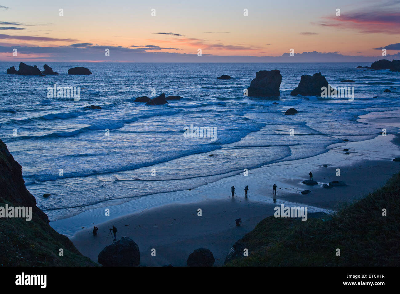 Photographers silhouetted on Bandon Beach at sunset with seastacks on the Pacific Ocean coast of Bandon Oregon Stock Photo