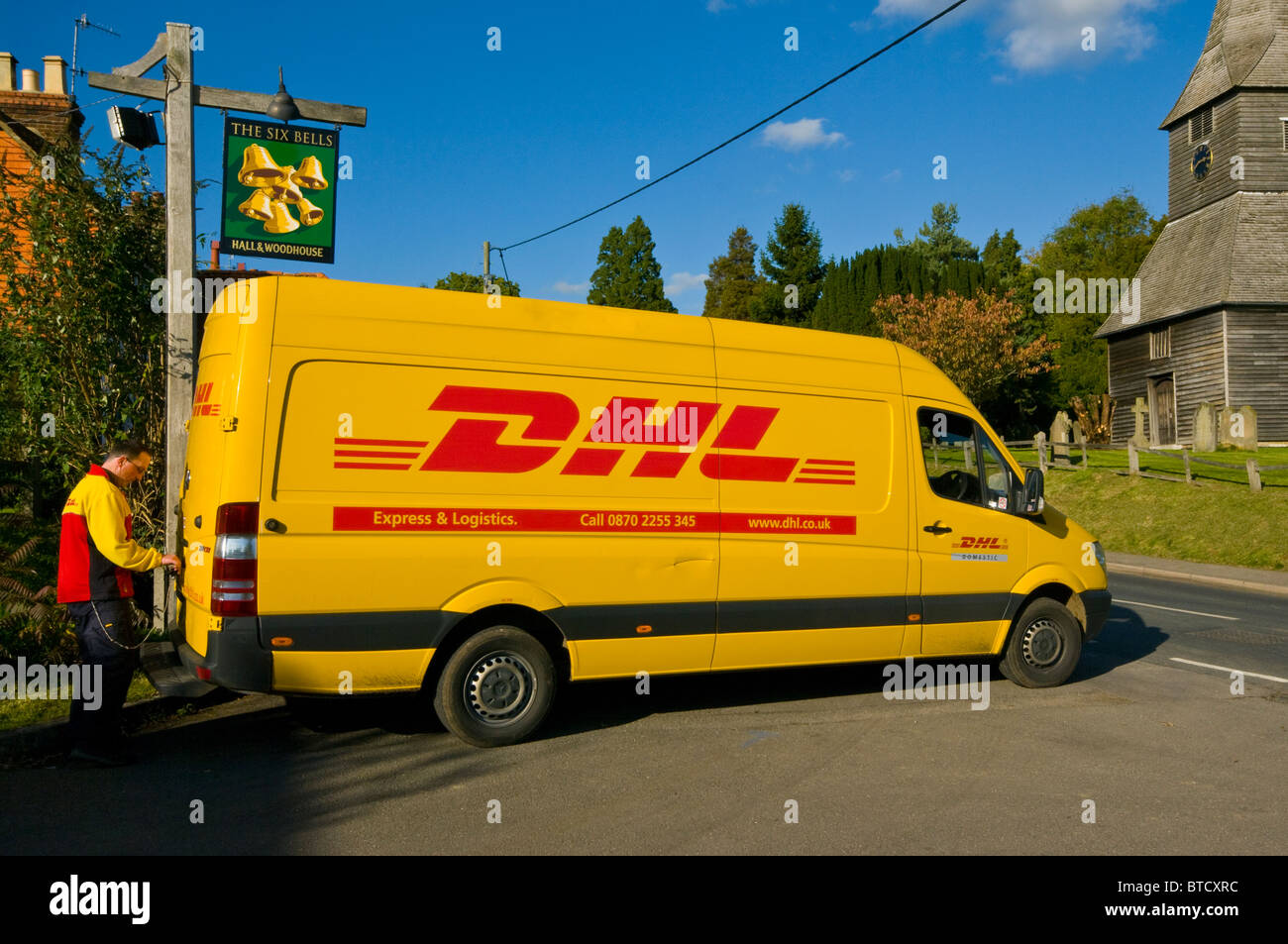 Driver In Uniform Opening The Rear Door Of A Yellow DHL Delivery Van