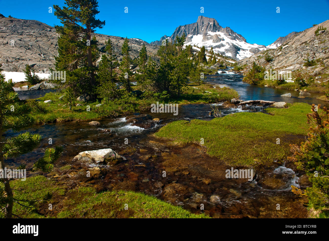 Stream flowing through green meadow below Banner Peak and Thousand Island Lake, Sierra Nevada Mountains, California Stock Photo