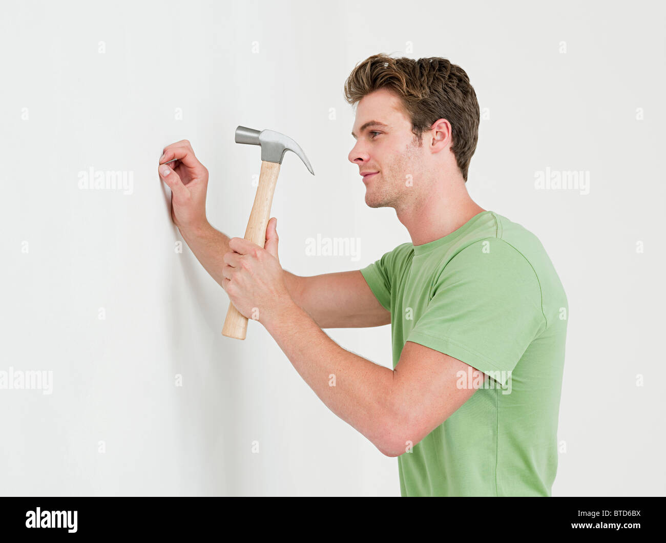Young man hammering nail into wall Stock Photo - Alamy