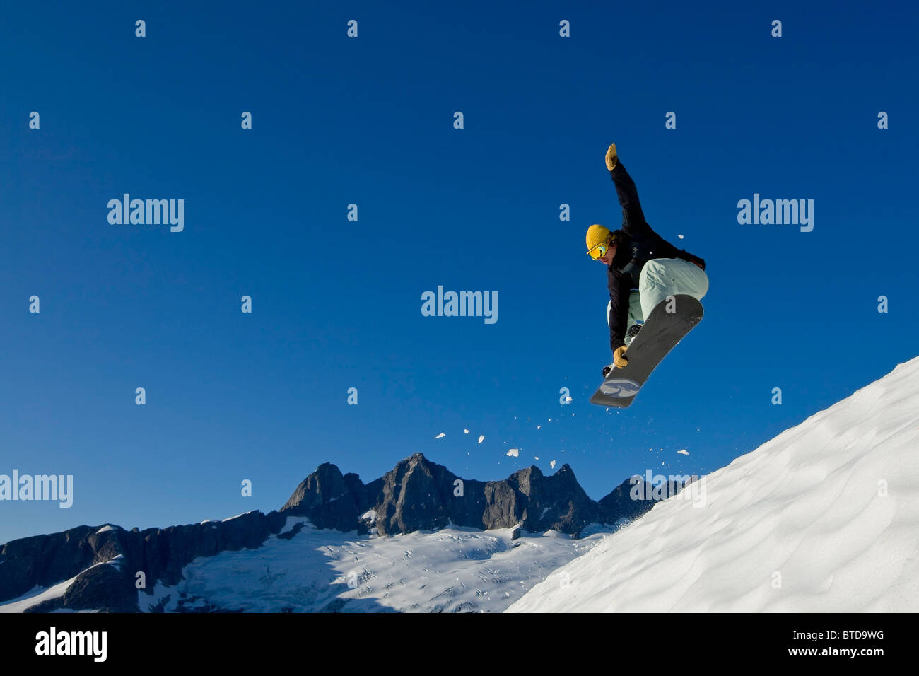 Snow boarder makes a jump on slopes in the Juneau area with Mendenhall Glacier and Towers in the background, southeast, Alaska Stock Photo