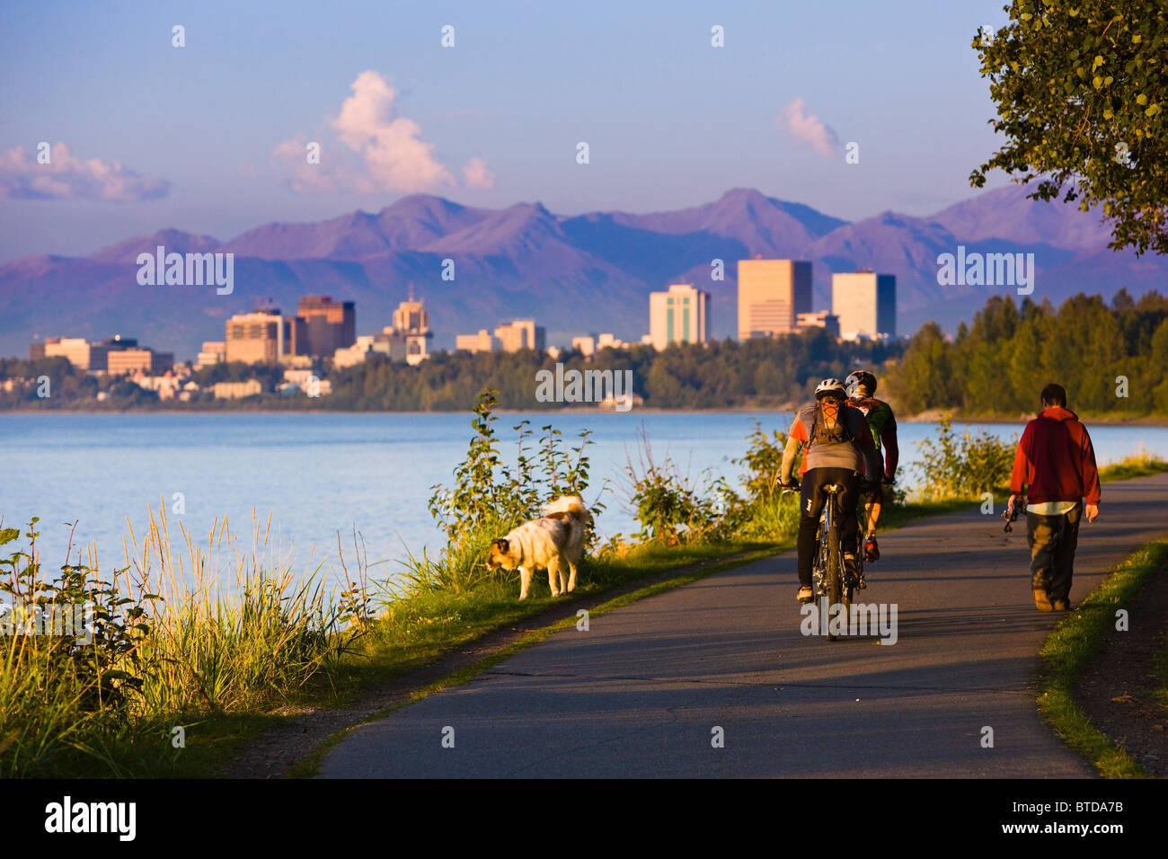 People jogging, walking and biking on the Coastal Trail with downtown Anchorage in the distance, Anchorage, Alaska Stock Photo