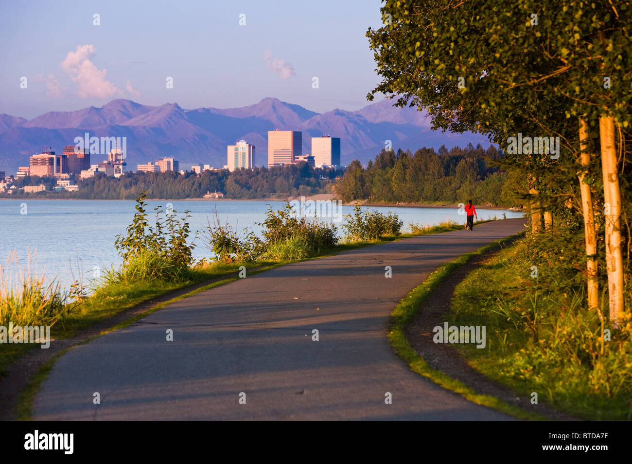 People jogging, walking and biking on the Coastal Trail with downtown Anchorage in the distance, Anchorage, Alaska Stock Photo