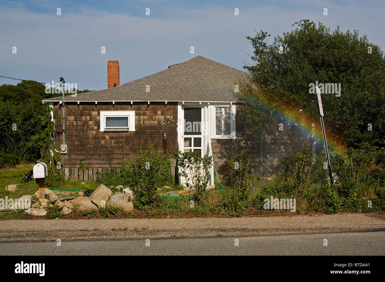 A rainbow  rises from the bushes in front of a tiny house Stock Photo