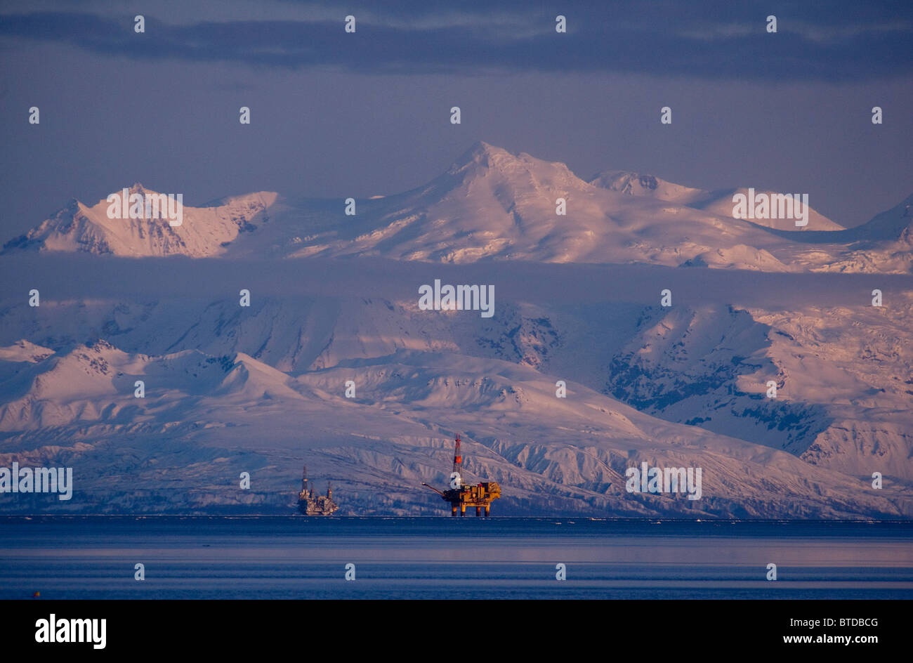 Three drill rigs in Cook Inlet with Mt. Spurr looming large in the background at sunset, Southcentral Alaska, Winter Stock Photo
