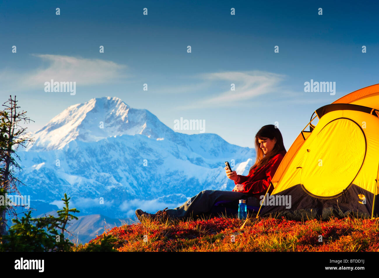 Woman talking on her cell phone while camping, Mt. McKinley in the background, Peters Hills, Denali State Park,  Alaska Stock Photo