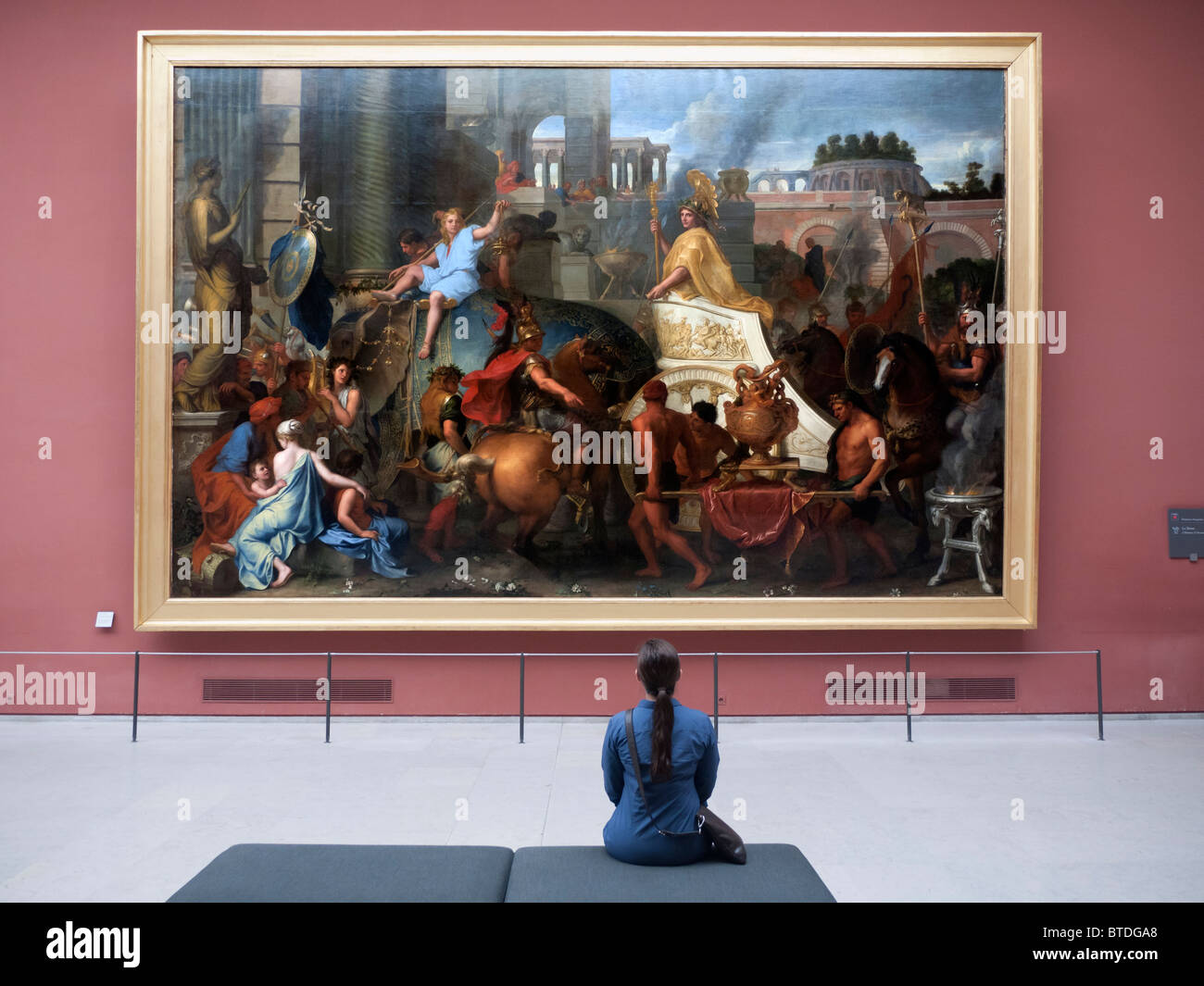 Woman looking at painting Entree d'Alexandre dans Babylone on L'Triomphe d'Alexandre by Charles Le Brun at The Louvre museum in Stock Photo