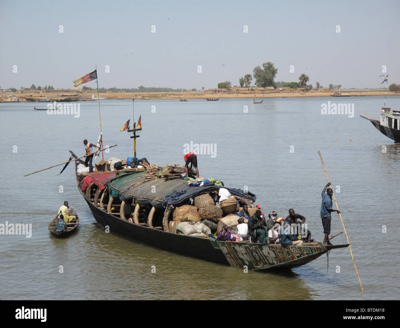A wooden boat with passengers and luggage on board being paddled across water Stock Photo