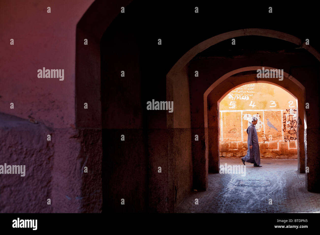 Local man walking along a Marrakech street viewed through a series of archways. Stock Photo