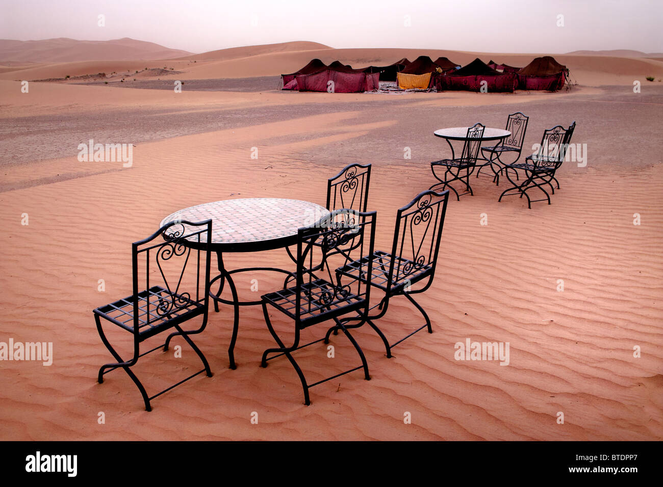 Two wrought iron patio tables with chairs at a rest stop in the Sahara, with traditional tents in the background Stock Photo