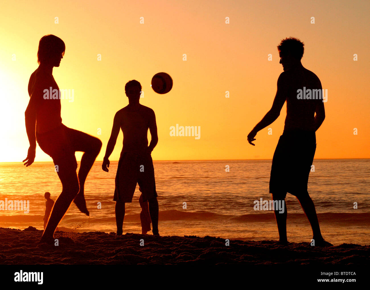 Young white adult men playing football on a beach at dusk Stock Photo