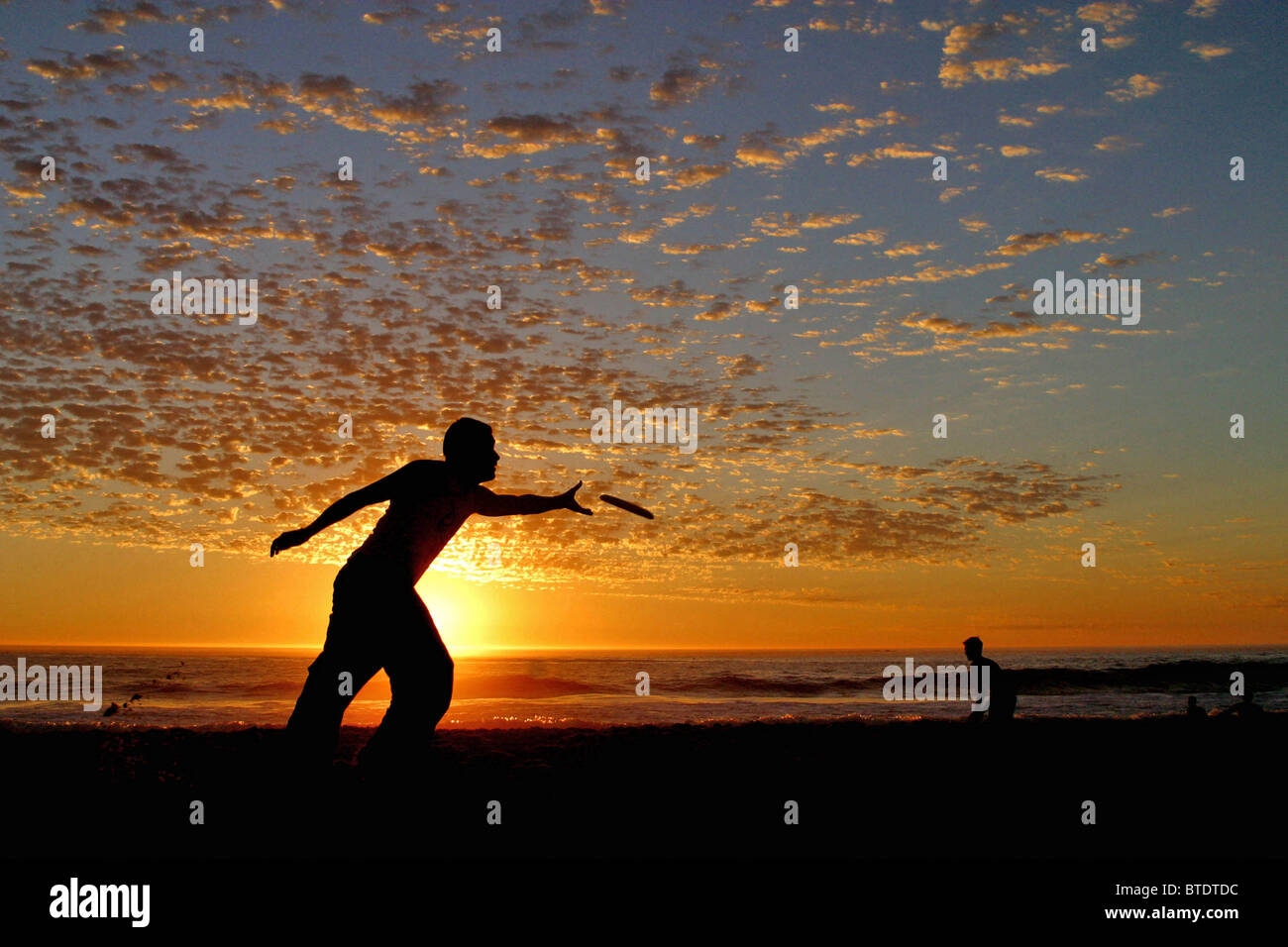 Two Frisbee players silhouetted on the beach at sunset Stock Photo